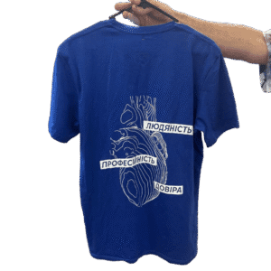 Blue t-shirt on a hanger with a white abstract line-art heart and Ukrainian words 'Професійність', 'Людяність', 'Довіра'.