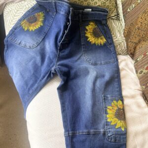 Blue denim jeans with large sunflower embroidery on back pocket and leg pocket detail, laid out on a couch.